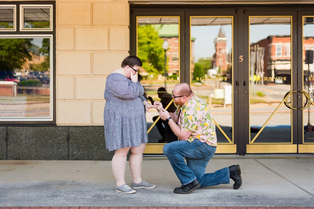 man kneels proposing to girlfriend outside Grand Theatre in Downtown Cartersville