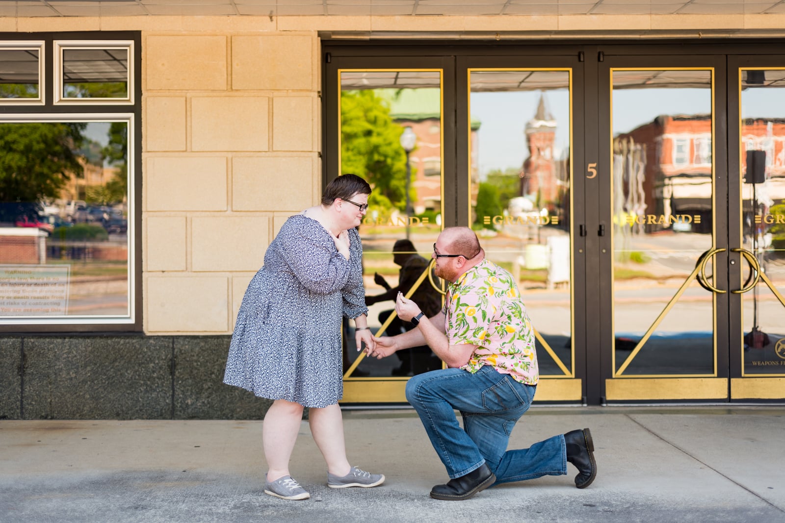 man kneels proposing to girlfriend outside Grand Theatre in Downtown Cartersville