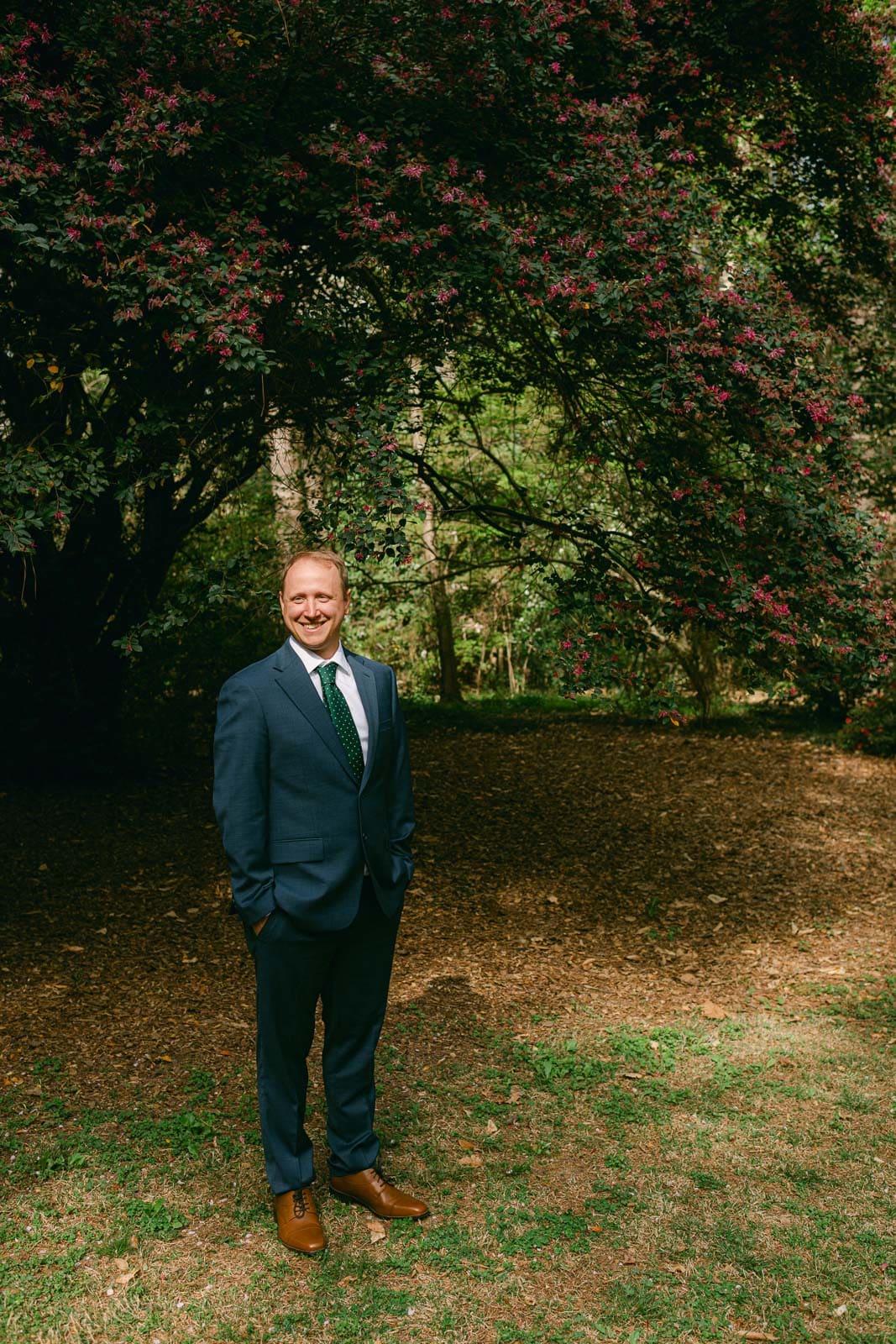 man stands in anvy suit in wooden at Woodlands Garden