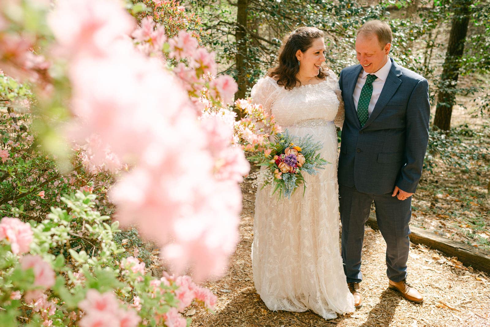 couple hugs in woods by pink trees at Woodlands Garden