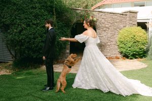 Groom about to turn around to see Bride for the first time while their dog jumps up towards Bride